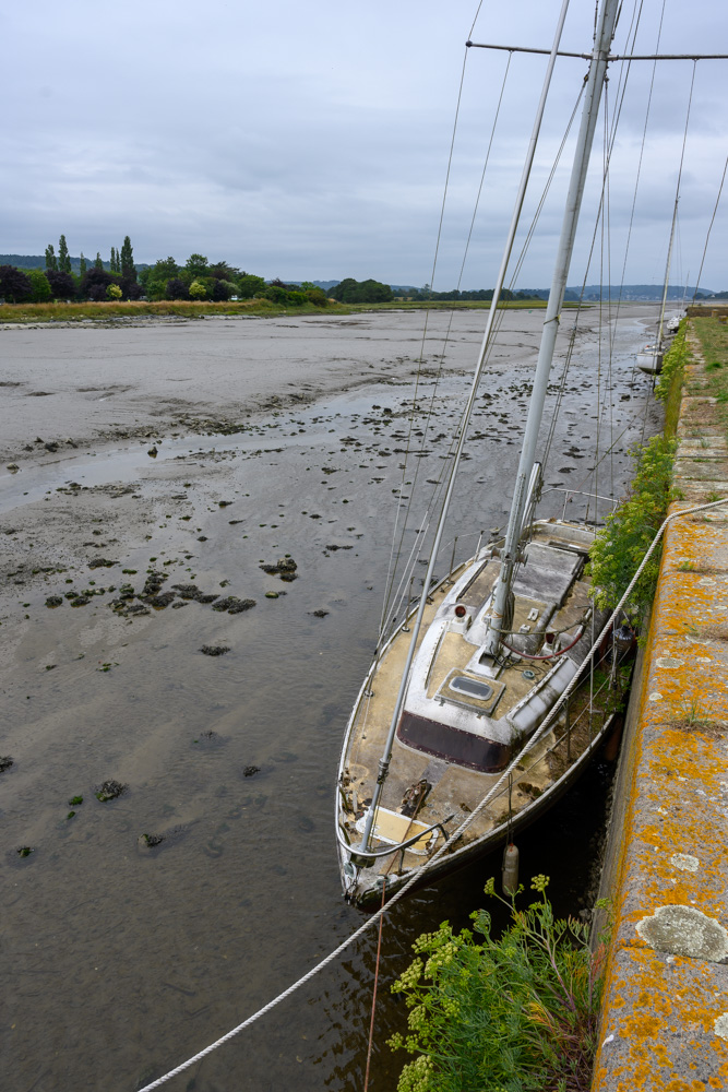 ein verwahrlostes Segelboot, das seit Jahren unbenutzt an einer Hafenmole hängt