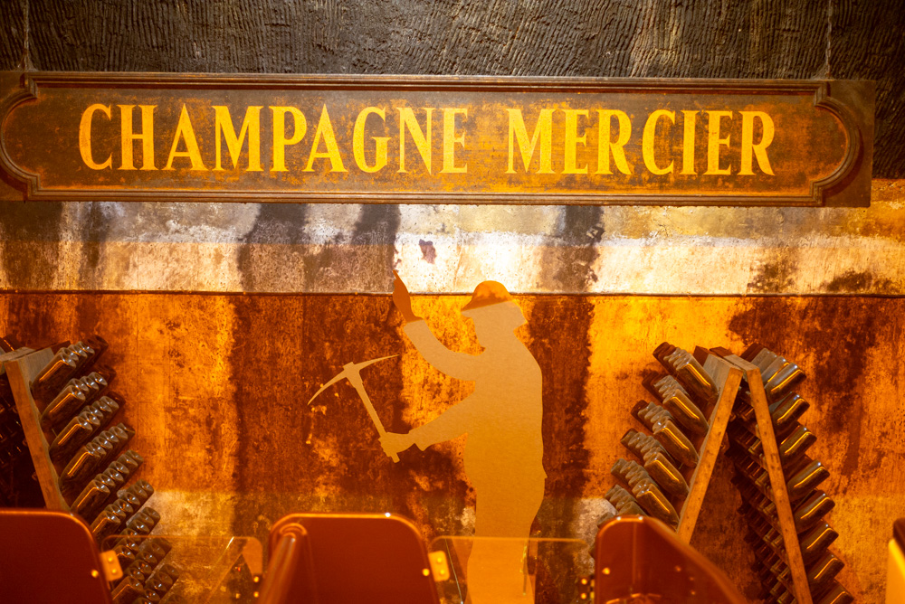 Rüttelbretter vor einer Männersilhouette, die auf ein Schild &ldquo;Champagne Mercier&rdquo; verweist
