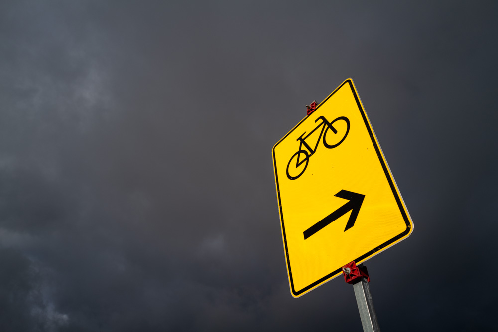 ein gelbes, reflektierendes Verkehrsschild für eine Radwegumleitung gegen einen nahezu schwarzen Gewitterhimmel