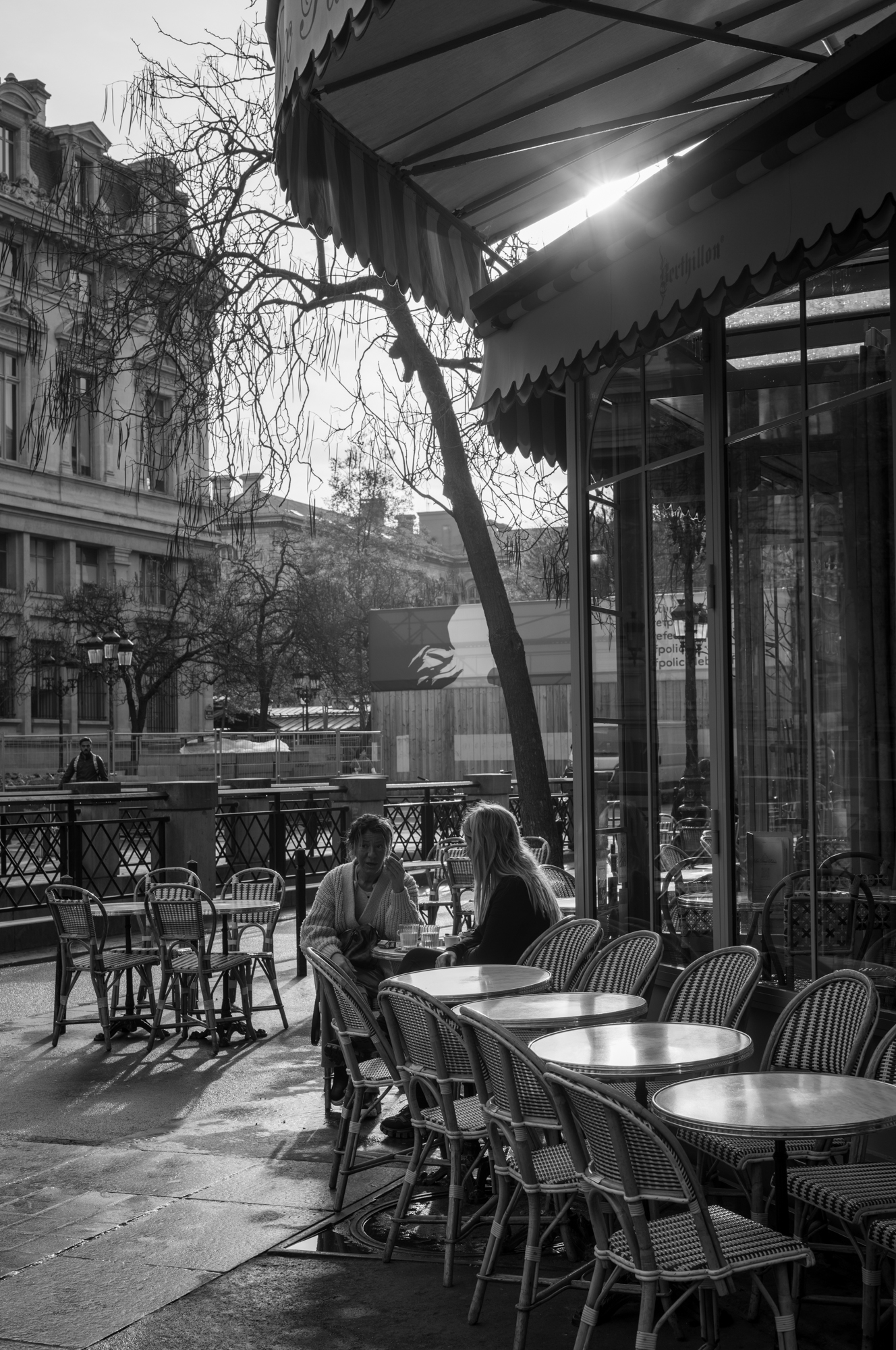 zwei Frauen sitzen in einem Straßencafé, die Sonne strahlt durch die Markisen