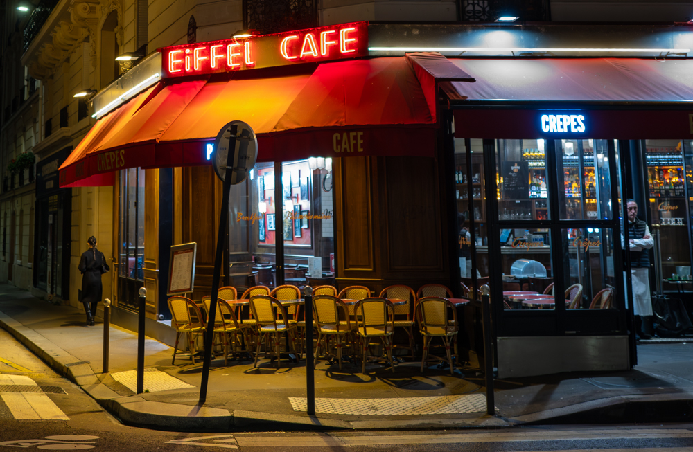 ein leeres Café, aus dem ein Kellner herausschaut und eine Frau auf der anderen Seite die Straße herunterläuft