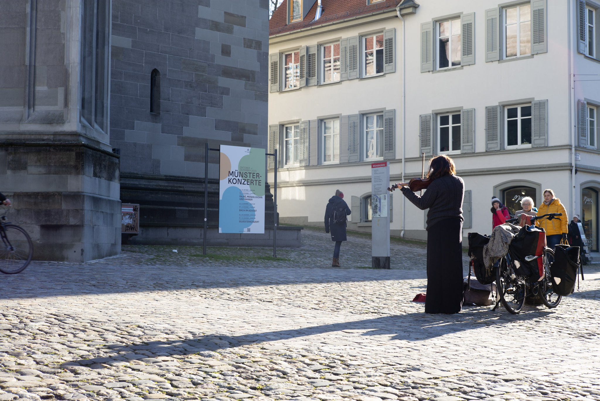 Straßenmusikerin mit Geige und Fahrrad auf dem Kopfsteinpflaster vor dem Konstanzer Münster