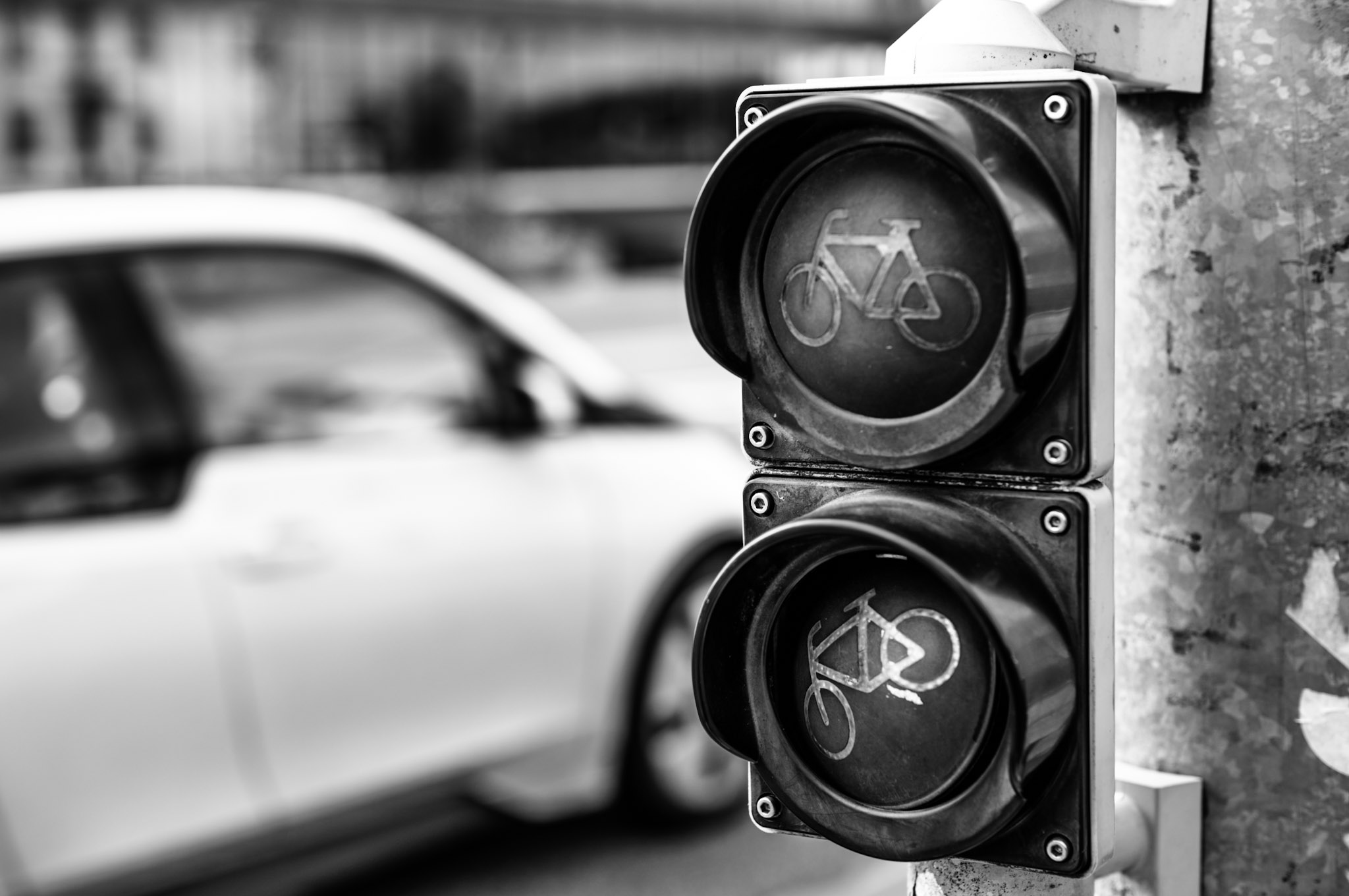eine Fahrradampel mit defektem unterem Glas, dahinter unscharf einn Auto im Straßenverkehr