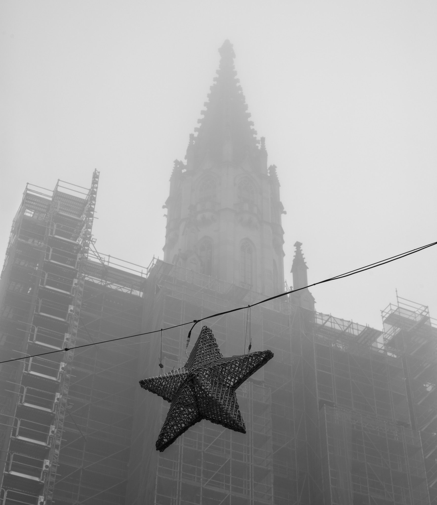 der Turm des Konstanzer Münsters, dessen Spitze langsam im Nebel verschwindet, im Vordergrund ein geflochtener Stern, der über einer Gasse als Schmuck hängt