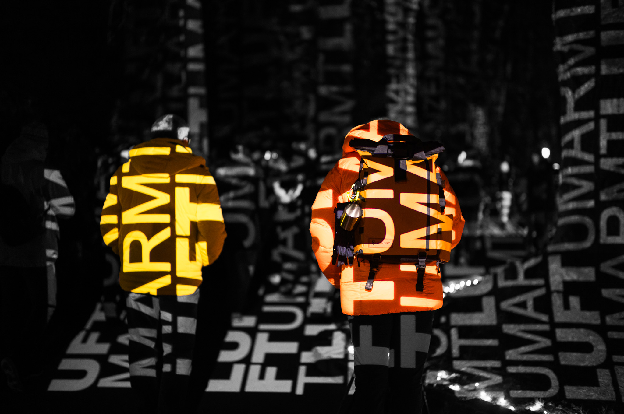 2 Personen in dicken, warmen Winterjacken, die von einer Buchstaben-Lichtprojektion beleuchtet werden